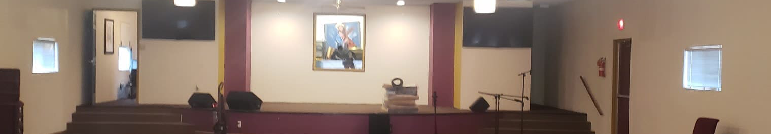 Empty church stage with central painting, microphone stands, and stacked chairs on the floor.