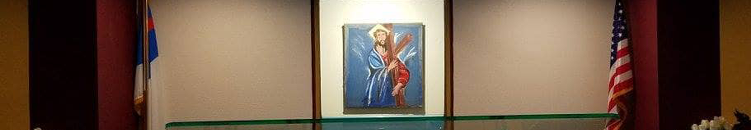 Framed painting of Jesus bearing a cross centered on a wall, with a glass shelf in front and flags on either side.